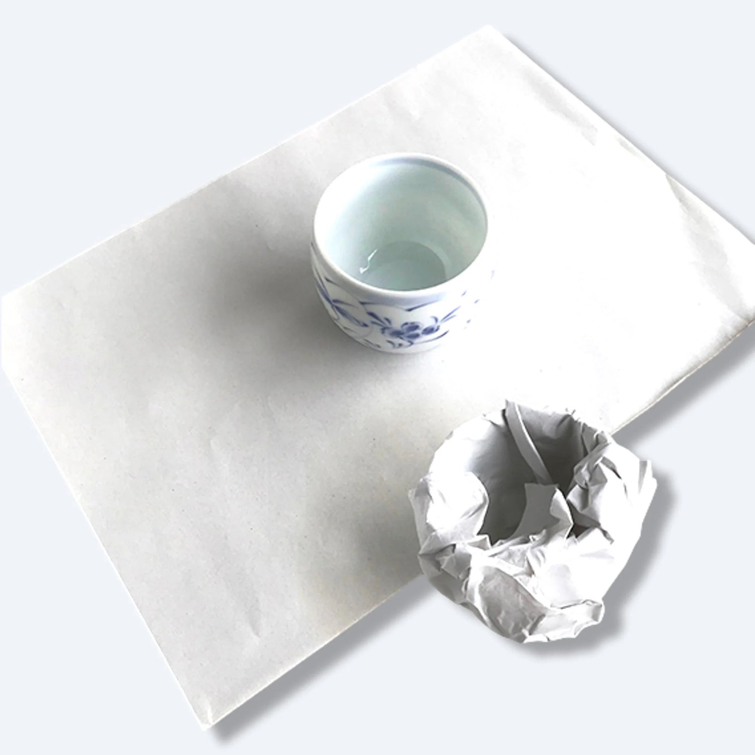 White newsprint packing paper sheet displayed with a ceramic cup and crumpled paper, illustrating protective wrapping use.