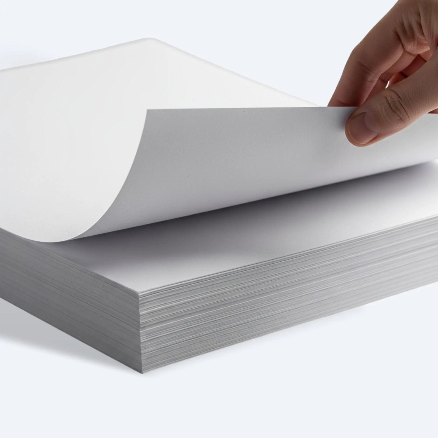 Hand lifting the top sheet of a newsprint paper ream, showing smooth, ink‑free surface for wrapping.