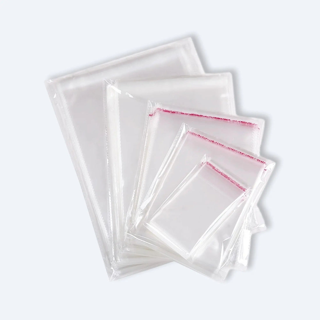 Fan display of clear OPP self‑adhesive bags in mixed sizes, each with red peel‑and‑seal strip for secure packaging.