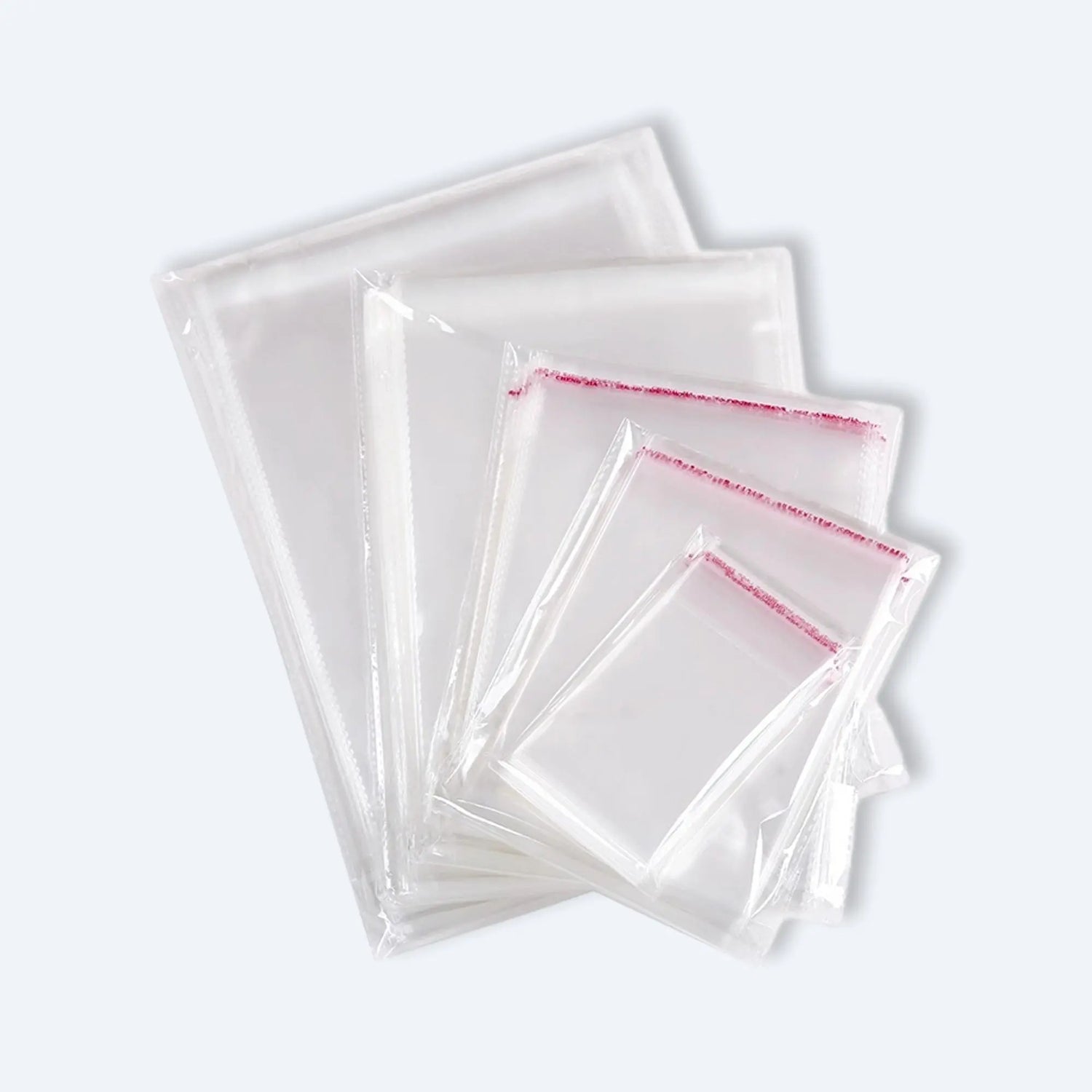 Fan display of clear OPP self‑adhesive bags in mixed sizes, each with red peel‑and‑seal strip for secure packaging.